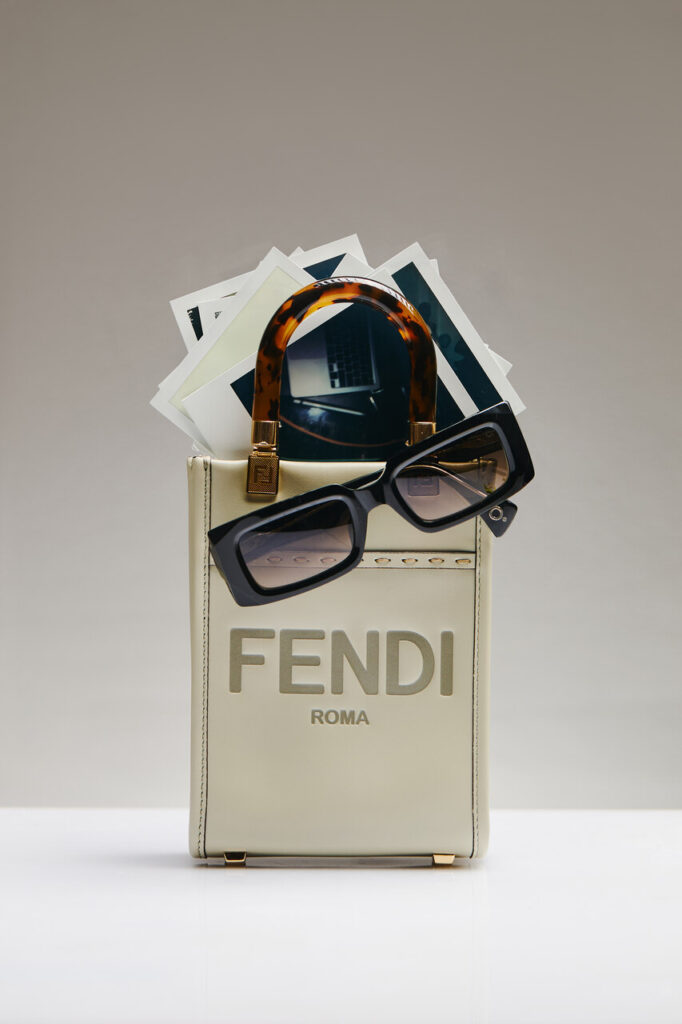 Bolsa Fendi bege com alça tartaruga e óculos pendurados, destacando luxo e estilo das melhores marcas de bolsas femininas, em composição minimalista com fotos instantâneas e fundo neutro.