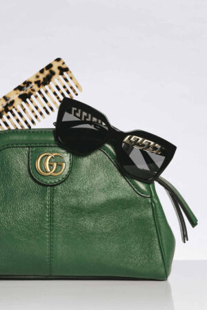Bolsa Gucci verde com logo dourado “GG”, óculos pretos e pente estampado compõem cena fashion que exalta o luxo das melhores marcas de bolsas femininas, com estilo e atitude.