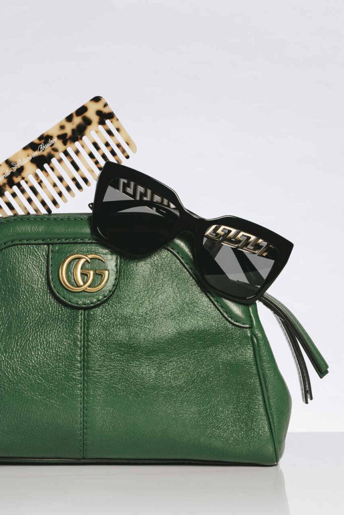 Bolsa Gucci verde com logo dourado “GG”, óculos pretos e pente estampado compõem cena fashion que exalta o luxo das melhores marcas de bolsas femininas, com estilo e atitude.