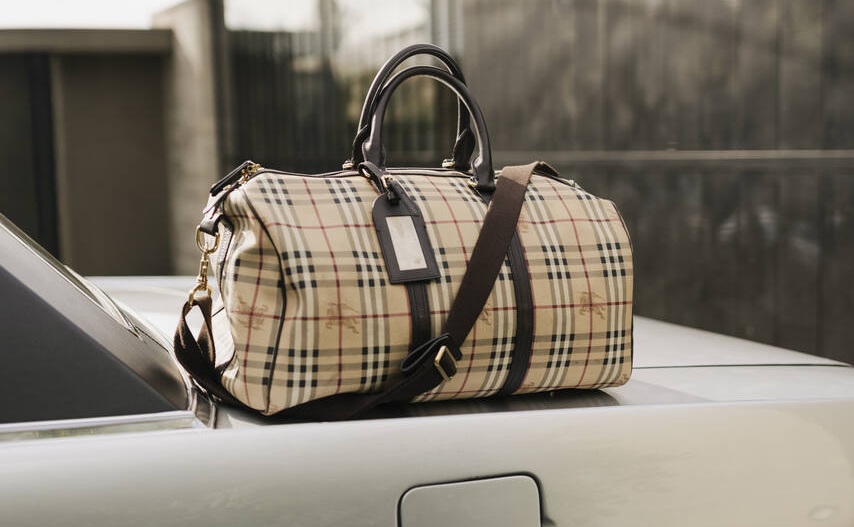 Bolsa xadrez sobre carro prateado, símbolo de viagem e estilo, conectando moda e automóveis às marcas de luxo feminina internacionais