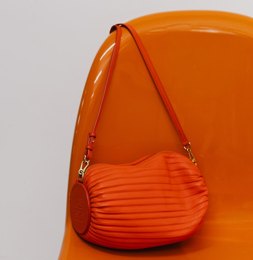 Bolsa laranja texturizada sobre cadeira monocromática, design sofisticado que remete ao universo das marcas de luxo feminina modernas