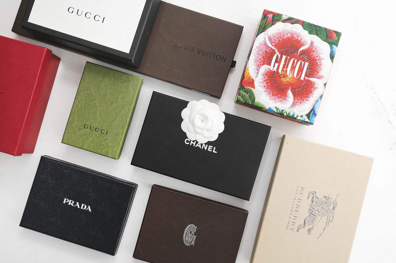 Caixas de diferentes marcas de alta costura, como Gucci, Chanel, Prada e Burberry, exibindo embalagens luxuosas e sofisticadas.