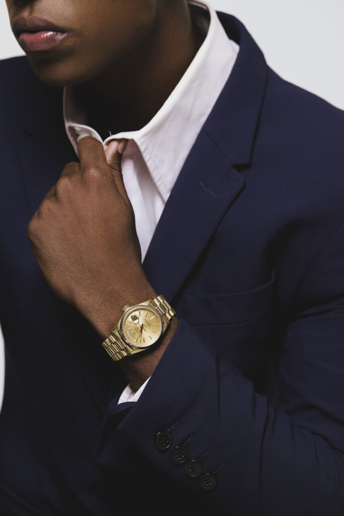 Homem ajustando camisa branca sob terno azul marinho, relógio dourado em destaque, transmitindo moda masculina 2026 com elegância profissional.
