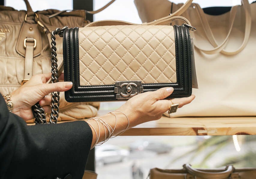Pessoa segurando bolsa Chanel bege com corrente, entre várias bolsas similares, destacando elegância das marcas de alta costura.