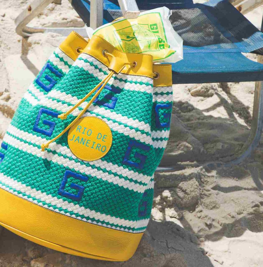 Bolsa de praia em crochê com detalhes amarelos e patch Rio de Janeiro, acessório vibrante da moda primavera verao 2026.